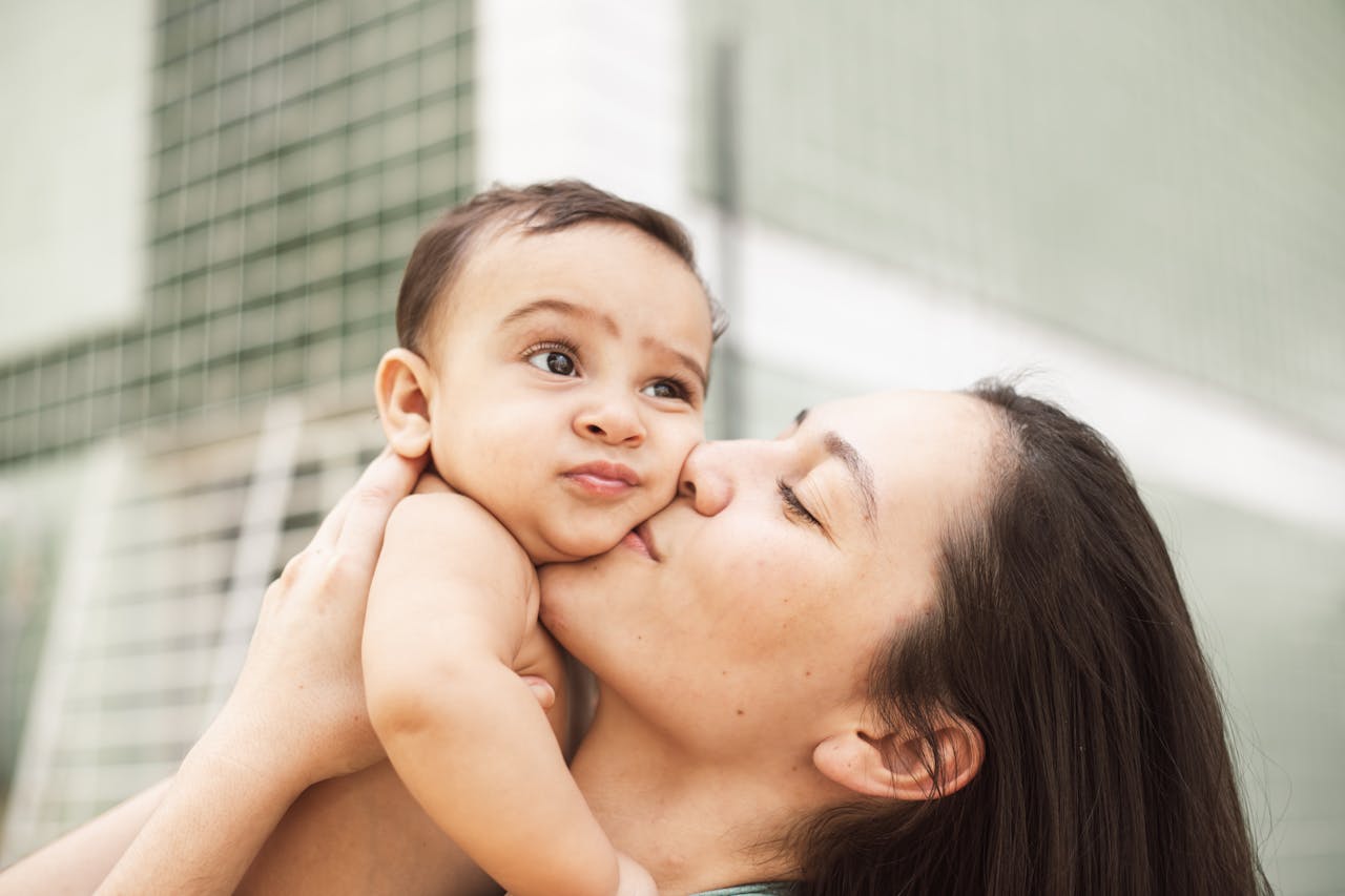 A loving mother kisses her baby, capturing a sweet moment of affection and intimacy indoors.