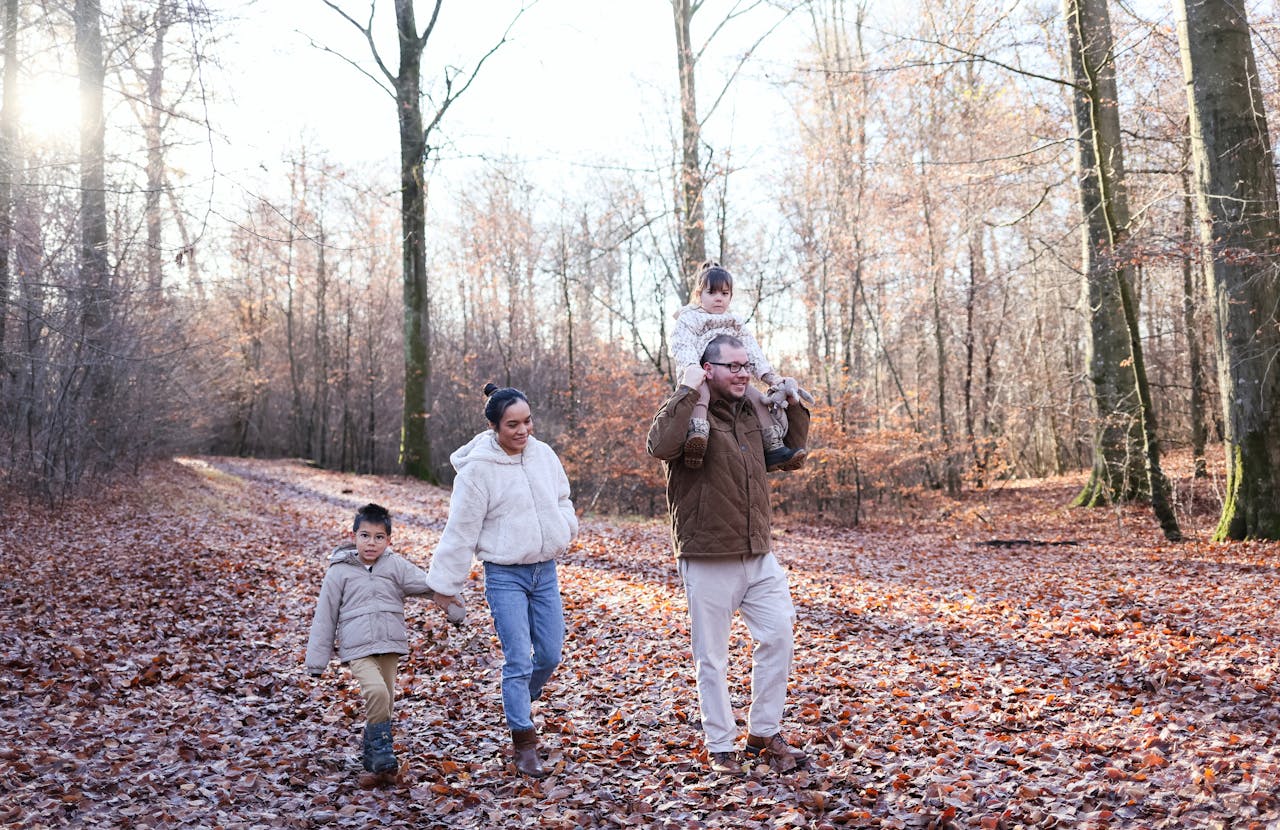 Family enjoying a walk in a forest with fallen leaves, capturing a warm, autumn moment.
