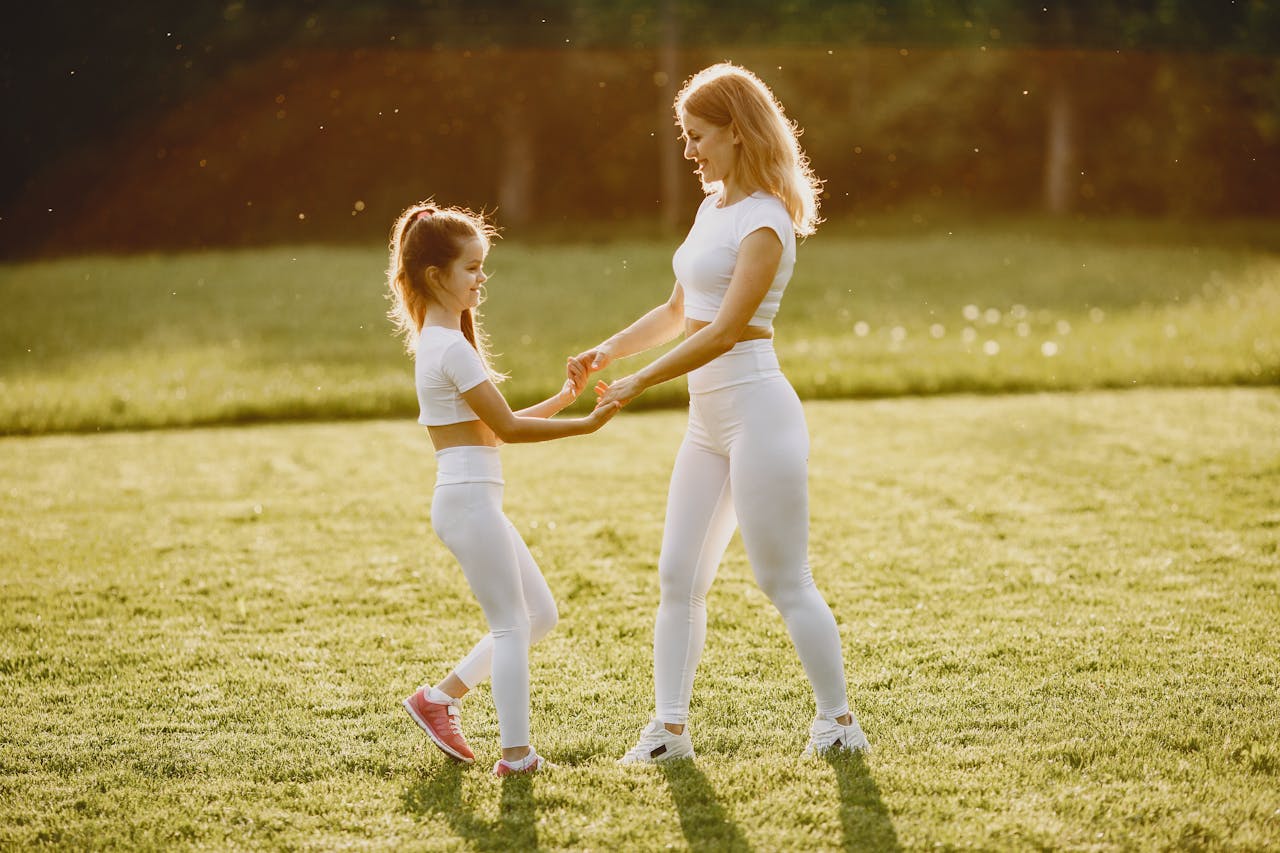 A mother and daughter in matching activewear enjoy playful bonding at the park during sunset.